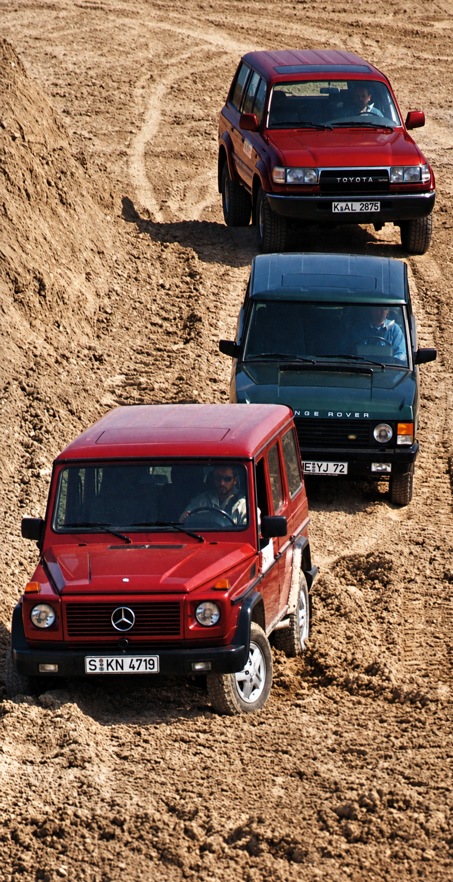 Le tre fuoristrada in fila sul terreno sconnesso: Mercedes in testa, Range Rover al centro e Toyota dietro — restauro assistito da IA dalla scansione originale